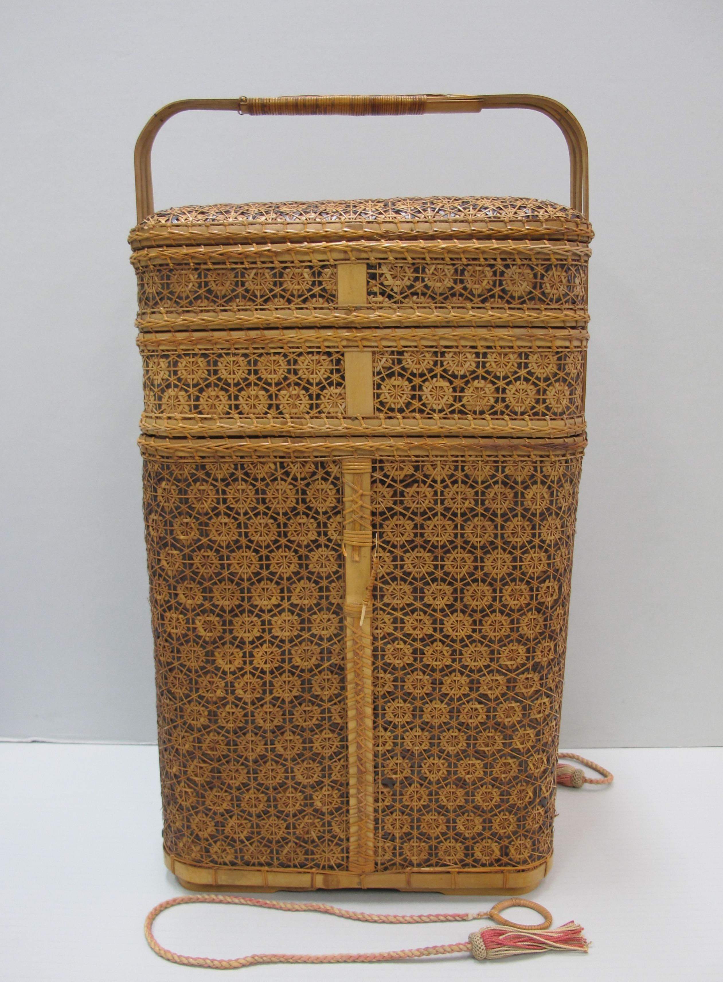Intricately woven bamboo basket with three tiered compartments, a lid, handle and two silk ties with tasseled ends.